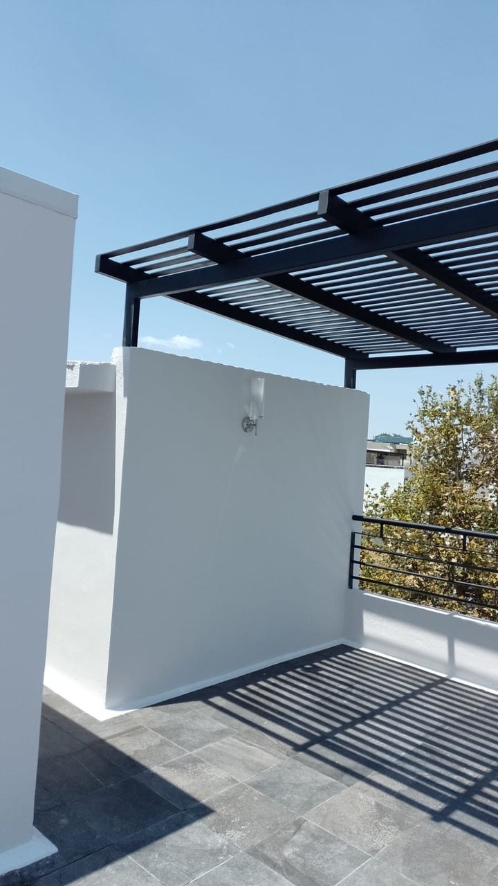 Pérgola metálica sobre terraza con muro blanco y acabado en negro